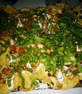 BBQ Spiced cheken  atop tortilla chips with black beans, diced red onions, diced tomatoes, shredded lettuce, siracha sour cream, shredded cheese and guacamole
